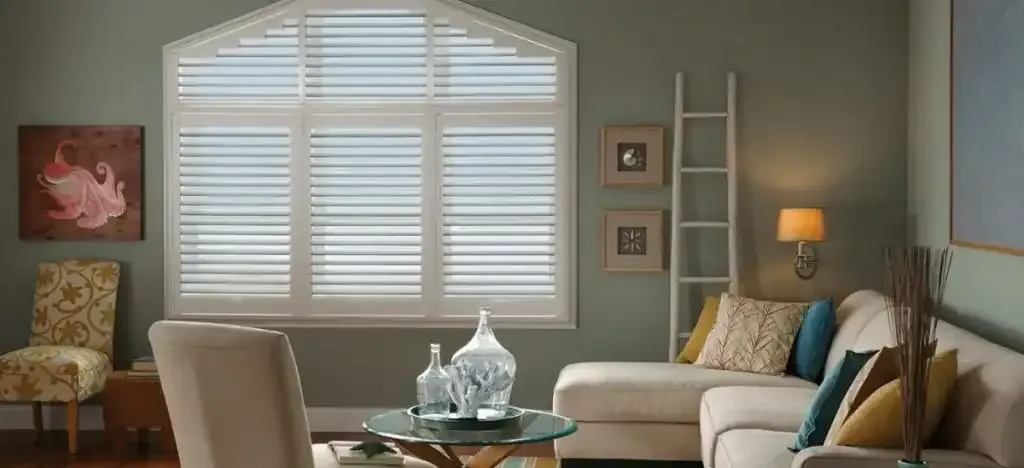 Living room with shuttered window, sofa, chair, and decorative items.